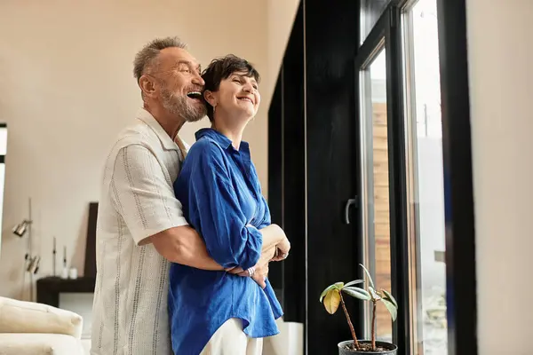 A cheerful couple embraces warmly at home, enjoying each other's company by the window. — Stock Photo