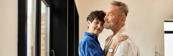 A cheerful middle-aged couple embraces, sharing love and happiness in their warm home, banner — Stock Photo