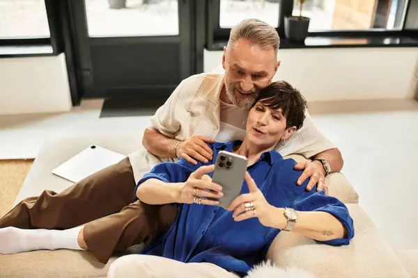 Coppia di mezza età si rilassa insieme sul divano, condividendo momenti di gioia durante l'utilizzo di uno smartphone. — Foto stock