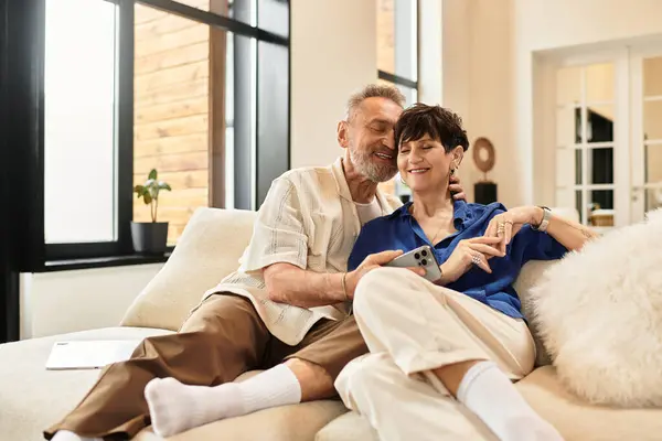 Marito e moglie di mezza età condividono un momento gioioso mentre guardano un dispositivo insieme al chiuso. — Foto stock
