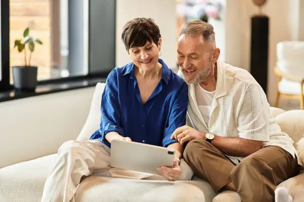 A happy couple enjoys time together, looking at a tablet on their cozy couch. — Stock Photo