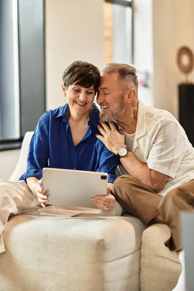 Un marito felice e moglie godono di tempo di qualità insieme, esplorando il loro tablet in un accogliente soggiorno. — Foto stock