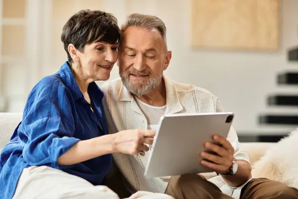 Joyful couple enjoys sharing moments together while exploring their tablet in a warm home setting. — Stock Photo
