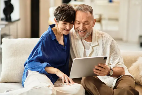 A cheerful married couple enjoys quality time at home, engaged with a tablet and sharing smiles. — Stock Photo