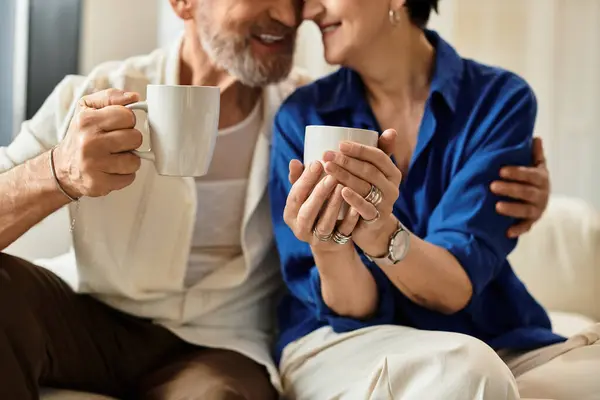 A happy middle-aged couple shares a warm moment at home, sipping coffee and smiling at each other. — Stock Photo