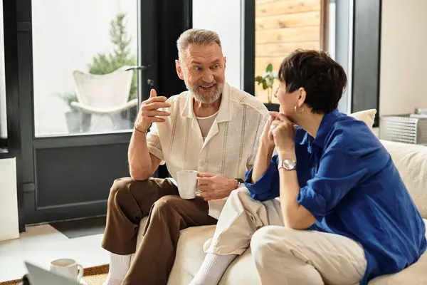 A cheerful middle-aged couple enjoys conversation and tea in their welcoming living space. — Stock Photo