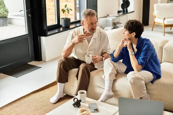 A happy couple enjoys a warm conversation over coffee while relaxing on their sofa. — Stock Photo