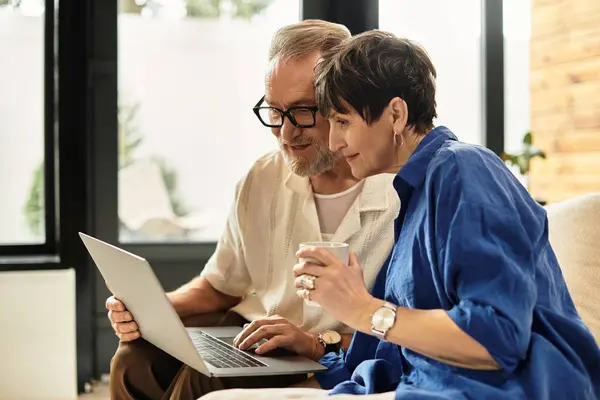 A happy couple sits close, sharing a moment as they explore their laptop with coffee. — Stock Photo