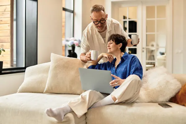 Un marito e una moglie felici condividono un momento accogliente mentre utilizzano un computer portatile nel loro elegante soggiorno. — Stock Photo