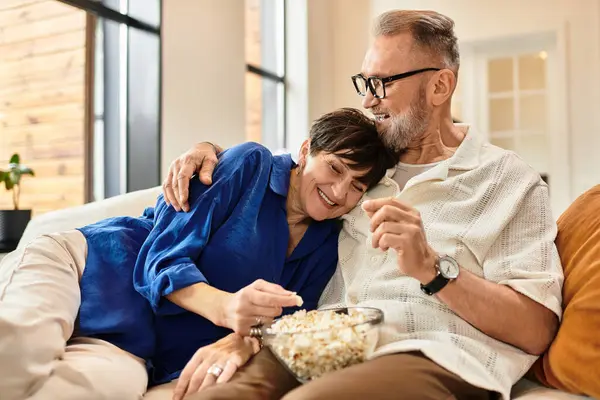A happy couple relaxes on the couch, sharing laughter and popcorn in their cozy living space. — Stock Photo