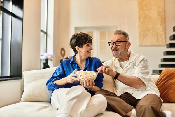 Coppia si rilassa insieme sul divano, condividendo risate e deliziosi popcorn nella loro accogliente casa — Foto stock