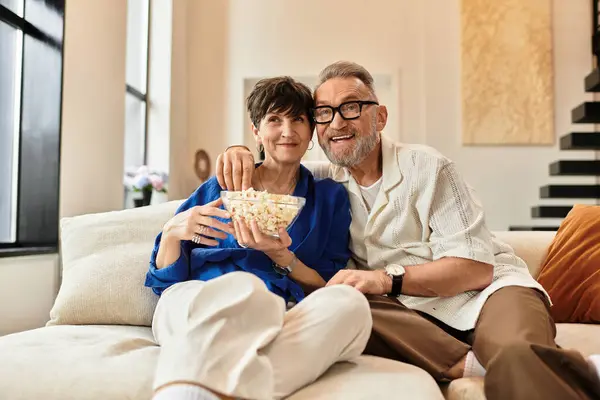 A married couple relaxes on the couch, sharing laughter and popcorn in their cozy living room. — Stock Photo