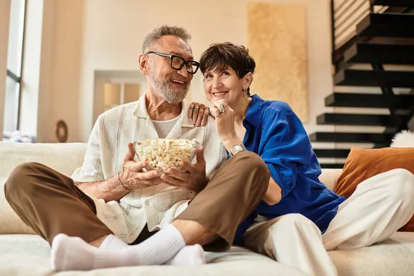 Couple enjoys a cozy evening on the couch, sharing laughter and snacks together at home. — Stock Photo