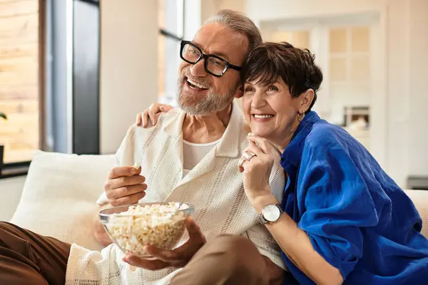 A joyful couple shares a beautiful moment at home, indulging in popcorn while watching a movie. — Stock Photo