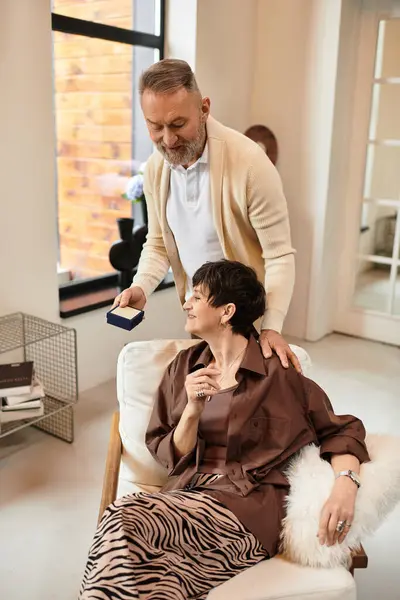 Middle aged husband surprises his joyful wife with a special gift in their inviting living room. — Stock Photo