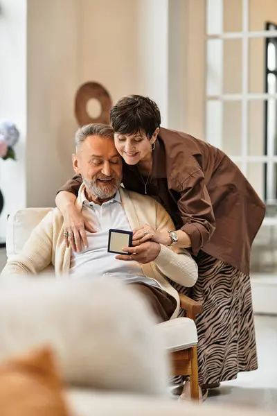 Middle aged couple shares a joyful moment at home, looking at present together. — Stock Photo