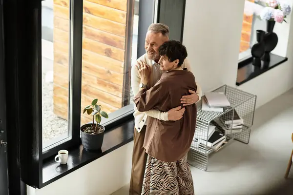 Una coppia gioiosa di mezza età abbraccia nel loro spazio di vita splendidamente progettato, celebrando l'amore. — Foto stock