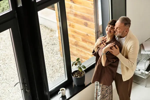 A joyful couple embraces lovingly at home near a cozy window, filled with warmth and happiness. — Stock Photo