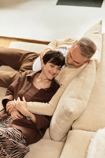 Una feliz pareja disfruta de la compañía del otro, sonriente y relajada en un sofá en su cálido hogar. - foto de stock