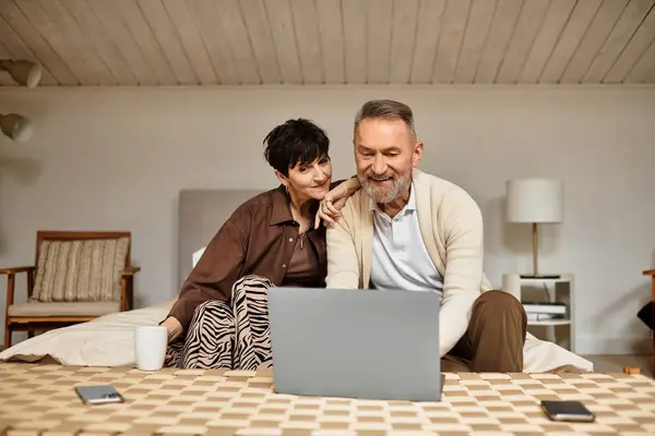 A cheerful couple engages in laughter and conversation while using a laptop at home. — Stock Photo