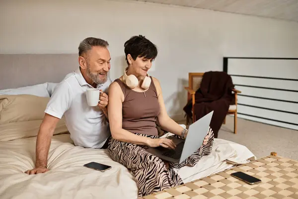 Happy couple sits on their bed, sharing a cozy moment while looking at a laptop with joy. — Stock Photo