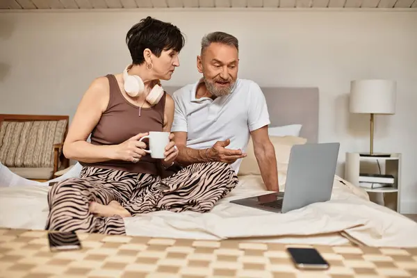 A joyful husband and wife share a cozy moment in their bedroom, engaging with a laptop. — Stock Photo