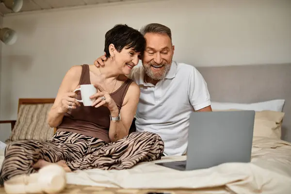 A happy couple enjoys quality time together, laughing and connecting over a laptop on their bed. — Stock Photo