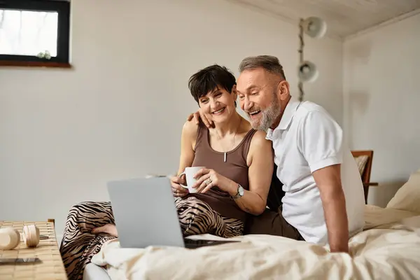 A joyous middle aged couple enjoys each other's company while browsing online together at home. — Stock Photo