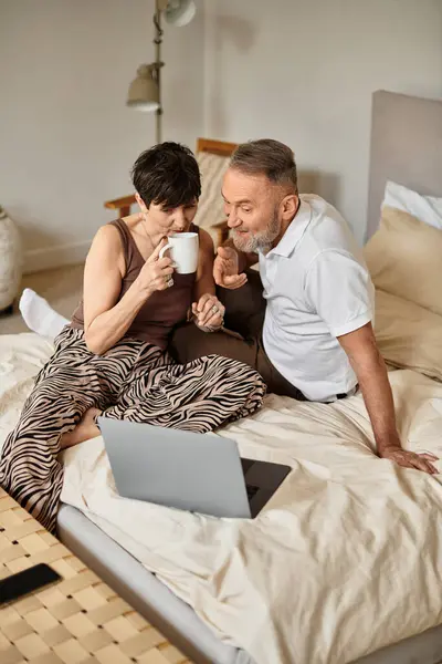 Una coppia di sposi gioiosi si rilassa insieme a letto, sorseggiando un caffè e godendo di un momento spensierato. — Foto stock