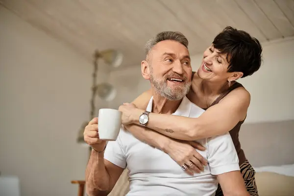 Coppia felice condivide un caldo abbraccio sorseggiando caffè insieme nella loro casa accogliente. — Foto stock