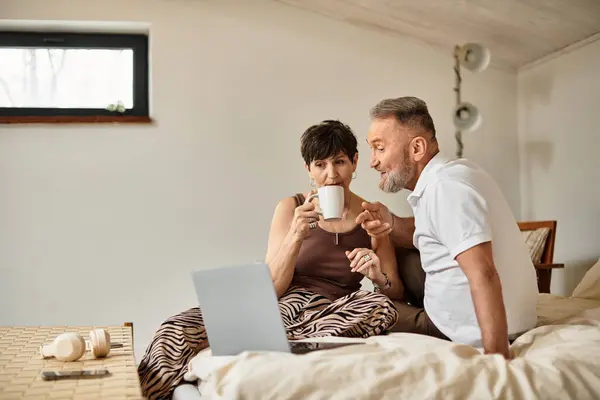 Middle aged couple sits together, sharing laughter and coffee in their cozy living space. — Stock Photo
