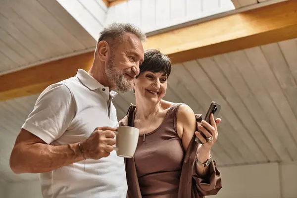 A joyful couple shares a light moment at home, enjoying coffee and a smartphone. — Stock Photo