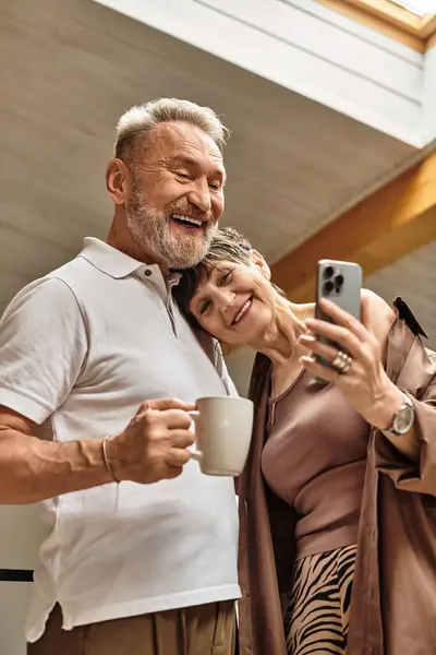 Um marido e uma esposa felizes compartilham o riso enquanto capturam uma selfie em sua casa quente. — Fotografia de Stock