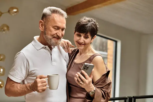 Um casal alegre de meia-idade compartilha um momento doce enquanto olha para um smartphone, calorosamente sorrindo. — Fotografia de Stock