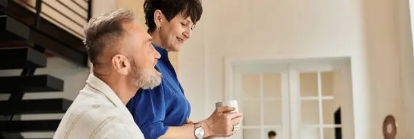 Middle aged couple shares joy while relaxing at home, bonding over warm beverages, banner — Stock Photo