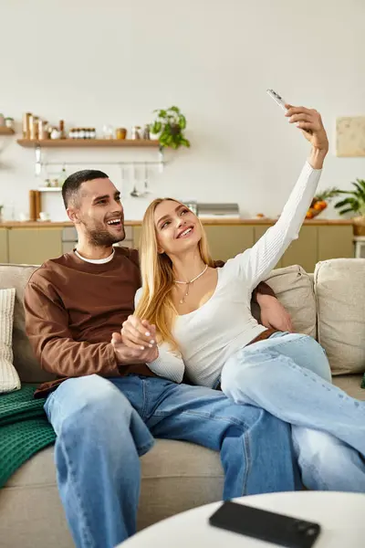 Couple cuddles on the couch, taking a playful selfie and enjoying their time together. — Stock Photo