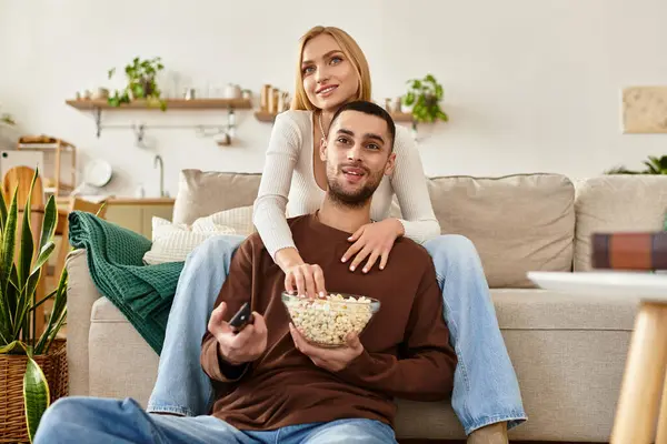 Una coppia ride e condivide popcorn insieme sul loro accogliente divano. — Foto stock
