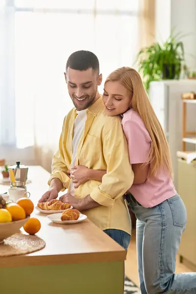 Coppia condivide un momento caldo mentre prepara la colazione con croissant e frutta fresca. — Foto stock