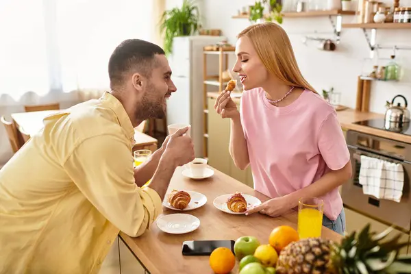 A couple shares smiles and treats while enjoying a joyful breakfast at home, radiating love. — Stock Photo