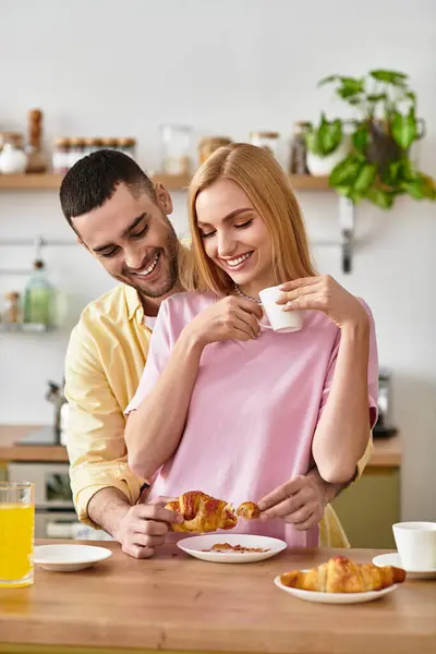 Un hombre y una mujer comparten un momento de amor mientras saborean croissants y café en su acogedora cocina. - foto de stock