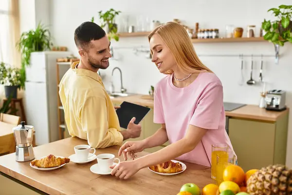 A man and a woman share a loving moment in their kitchen while enjoying coffee and pastries. — Stock Photo