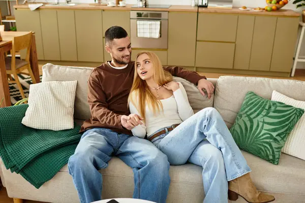 Una pareja amorosa disfruta de la compañía de los demás mientras se sientan juntos en un cómodo sofá en casa - foto de stock