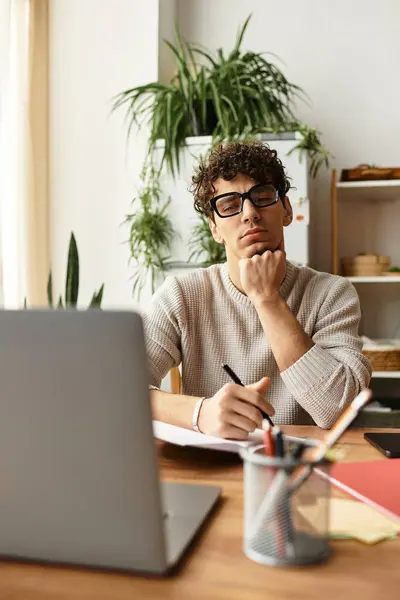 Thoughtful young man with glasses writes notes in a green, modern workspace. — Stock Photo