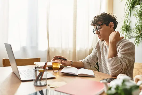 Handsome young man focuses on his studies, sipping tea at a quaint desk surrounded by greenery. — Stock Photo