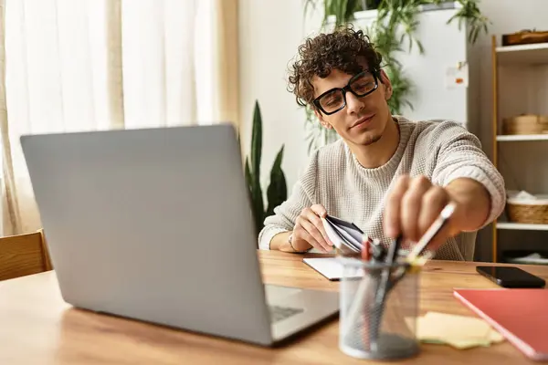 Un bel giovanotto si siede su una scrivania di legno, sistemando articoli di cancelleria mentre la luce del sole riempie la stanza.. — Stock Photo