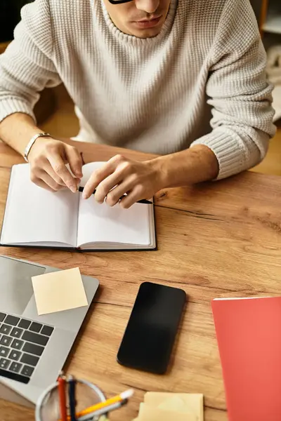 Ein stilvoller junger Mann wirft an seinem Schreibtisch Notizen, umgeben von kreativen Werkzeugen. — Stockfoto