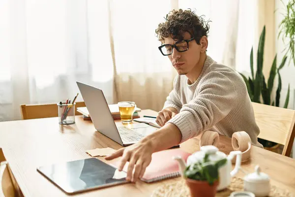 Beau homme dans des lunettes élégantes se concentre sur le travail à un bureau en bois lumineux au milieu de la verdure. — Photo de stock