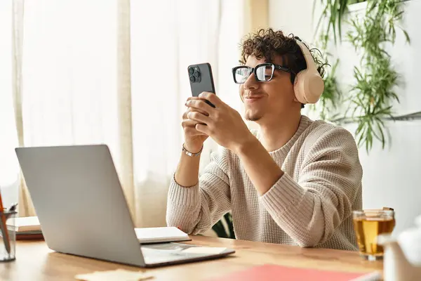 Un bel giovane uomo con i capelli ricci sorride mentre usa il suo smartphone in un accogliente spazio di lavoro. — Stock Photo