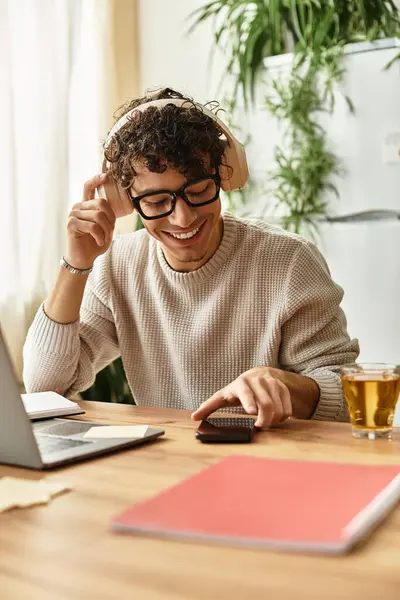 Man with curly hair and headphones smiles while using a phone during a productive afternoon. — Stock Photo