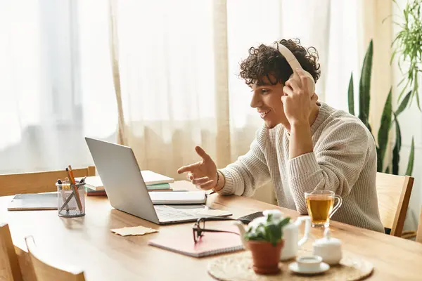Encantador joven se involucra con entusiasmo mientras trabaja en su computadora portátil en una habitación luminosa. - foto de stock